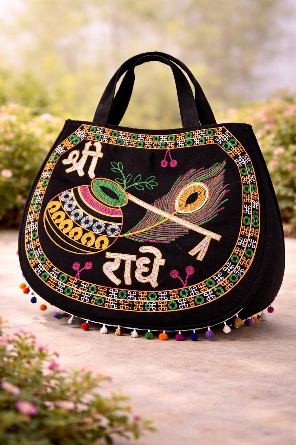 Black handbag with colorful embroidery and peacock feather design on a blurred natural background