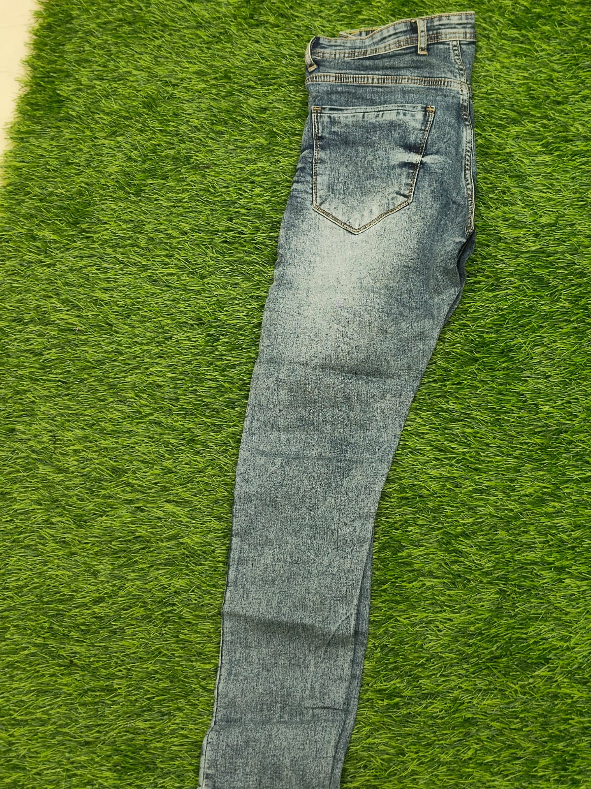 Folded pair of light blue jeans on a green grass
